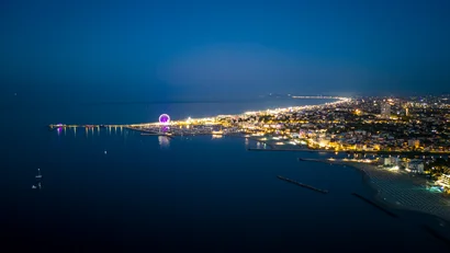 Veduta notturna della città costiera illuminata con ruota panoramica