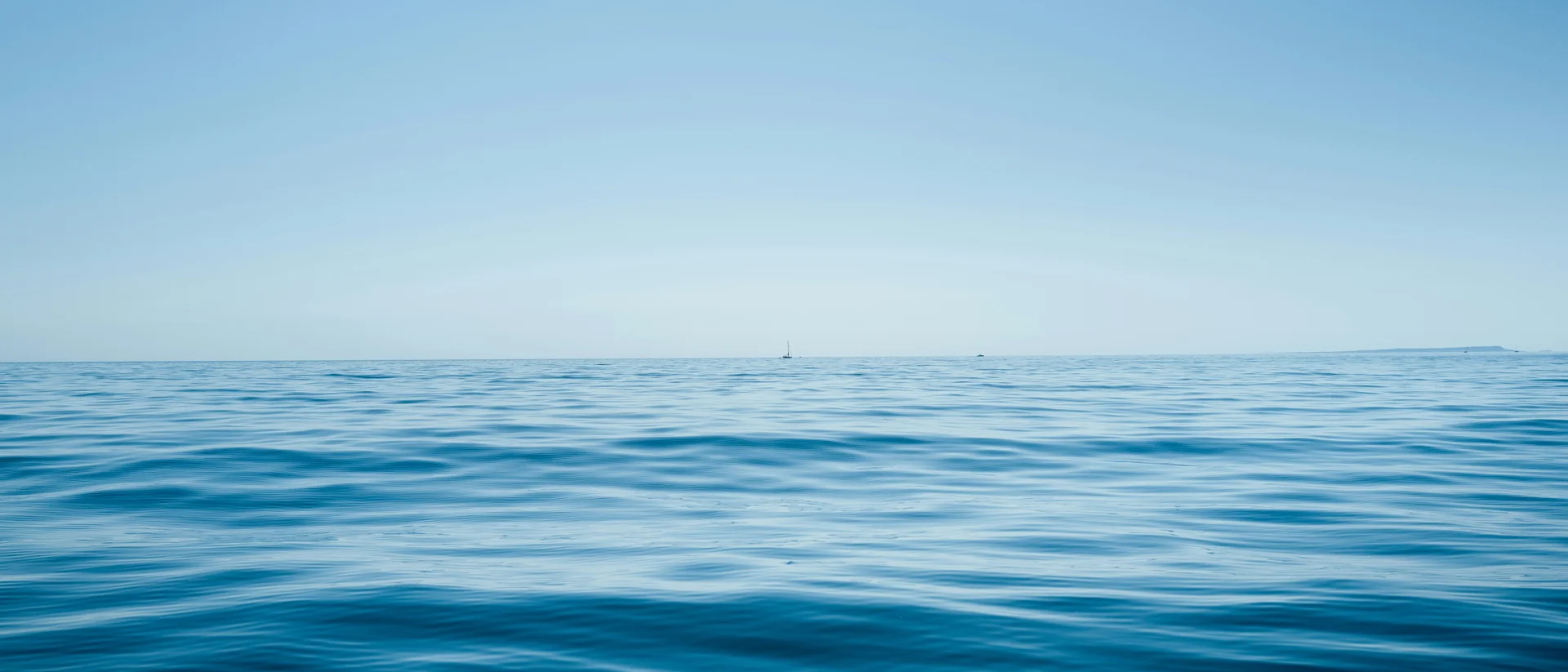 Oceano calmo con barca a vela lontana e cielo azzurro