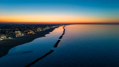 Vista aerea del lungomare al tramonto con luci della città e mare calmo.