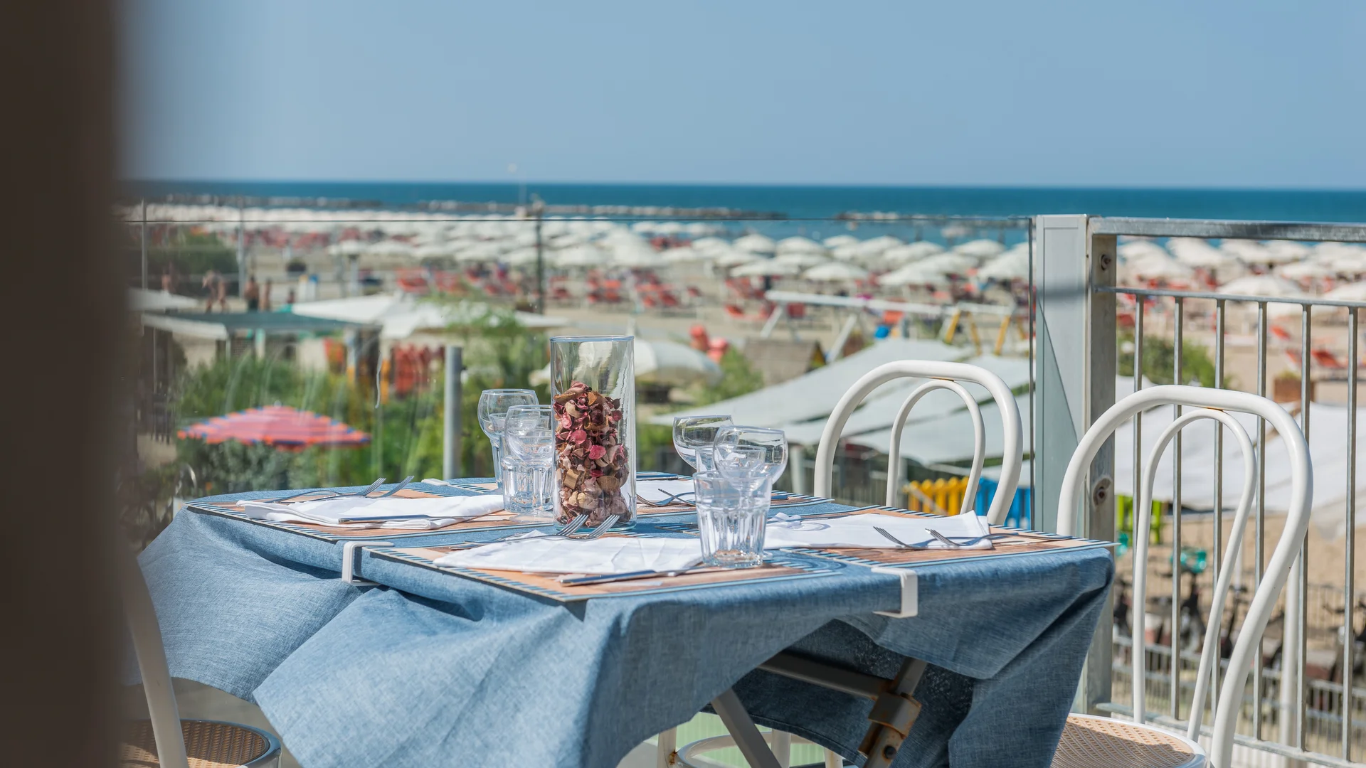 Tavolo apparecchiato con tovaglia blu su terrazza con vista sulla spiaggia e mare