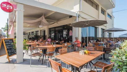 Tavoli e sedie in legno in un bar all'aperto con persone sedute