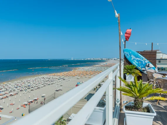 Vista dal balcone di una spiaggia affollata con ombrelloni colorati e mare blu
