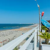 Vista dal balcone di una spiaggia affollata con ombrelloni colorati e mare blu
