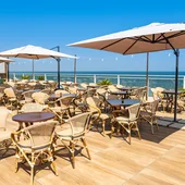 Terrazza ristorante con tavoli, sedie e ombrelloni vista mare.