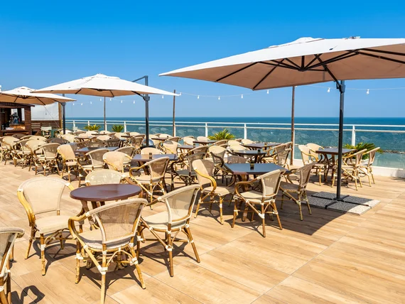Terrazza ristorante con tavoli, sedie e ombrelloni vista mare.
