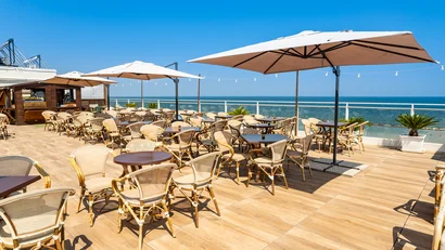 Terrazza ristorante con tavoli, sedie e ombrelloni vista mare.